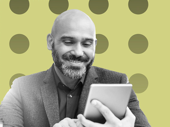 Black-and-white image of a person in a blazer holding and looking at a tablet device, shown from the chest up, set against a light green background with evenly spaced circular patterns.