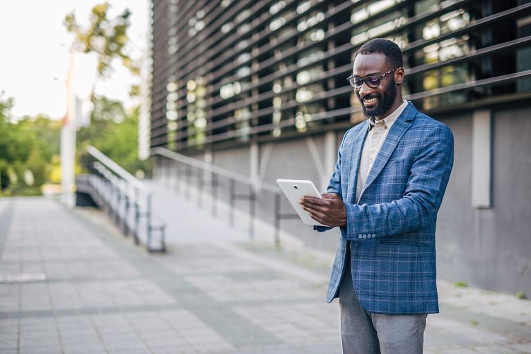 businessperson standing outside a building reading from a tablet device