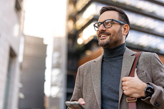 Smiling businessman walking in the city with his smartphone