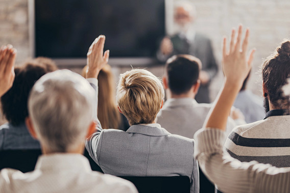 Back view of a businessman raising his hand to ask a question while attending a business seminar with his colleagues in board room.