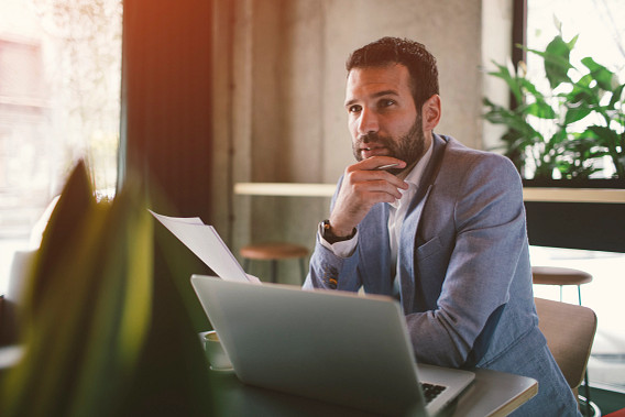 Businessman working in cafe. Sitting, holding documents and using laptop